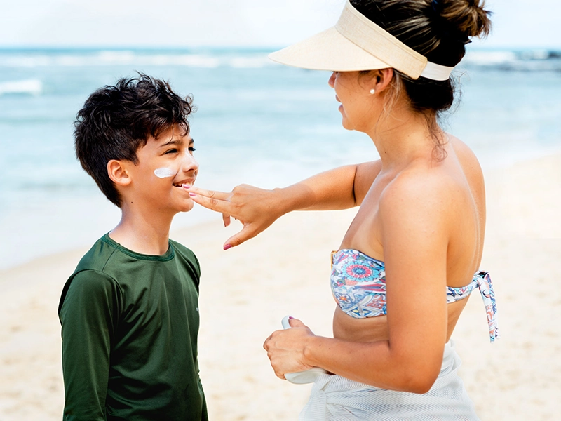 Mom applying sunscreen to her son while they are at the beach