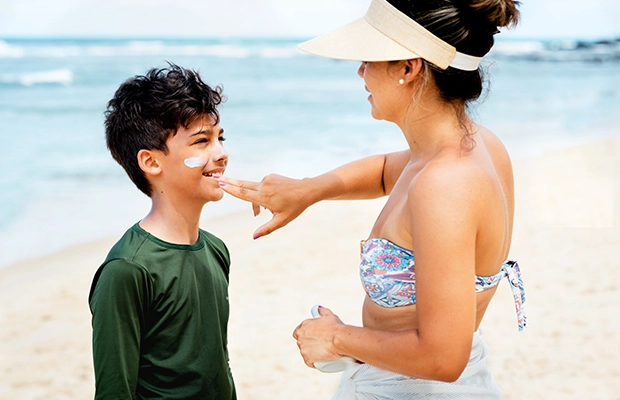 Mom applying sunscreen to her son while they are at the beach