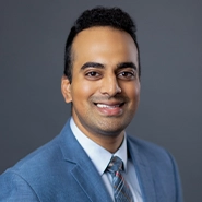 A headshot of a medical professional, he has on a blue coat