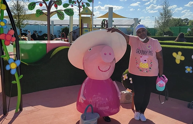 Woman wearing a Peppa Pig T-shirt posing next to a Peppa Pig statue.