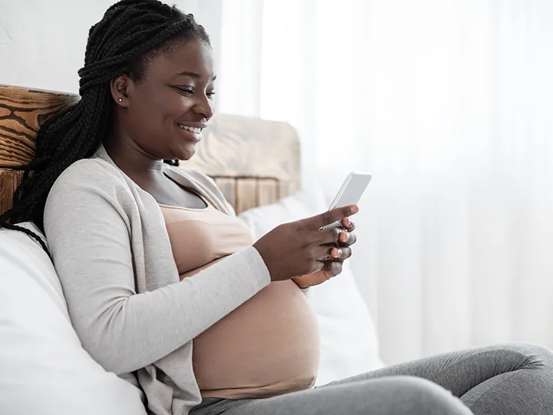 A woman sitting up in bed, she's using her mobile device, she is pregnant