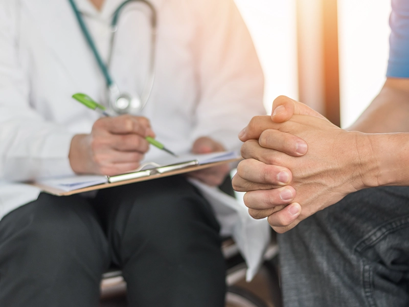 Close-up showing the knees and hands of two people sitting on a sofa and talking.