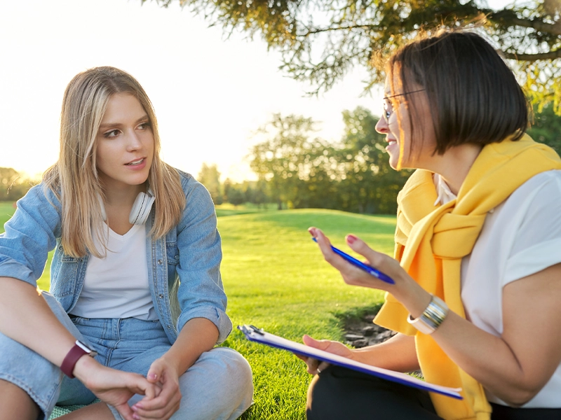 Two women talking while sitting on the grass in a park