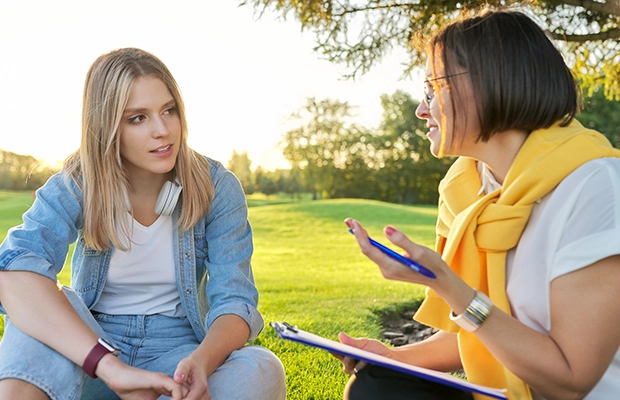 Two women talking while sitting on the grass in a park