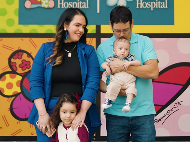 Photograph of a family with a colorful mural behind them.