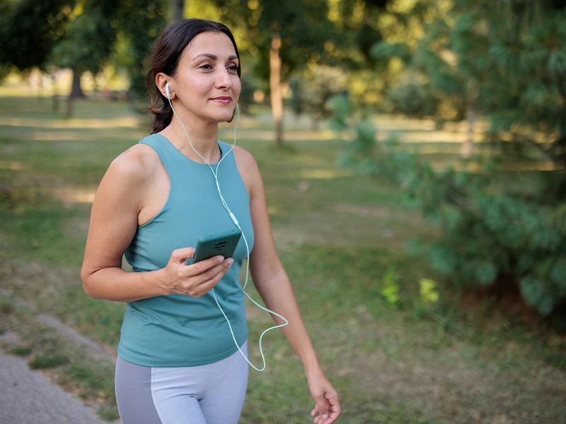 Woman in sportswear and short hair walking in the park while listening to something on her headphones