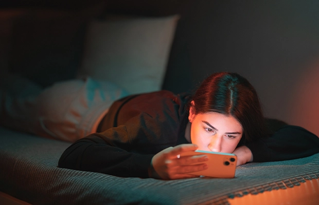 Teenage girl lying in bed looking at her cell phone