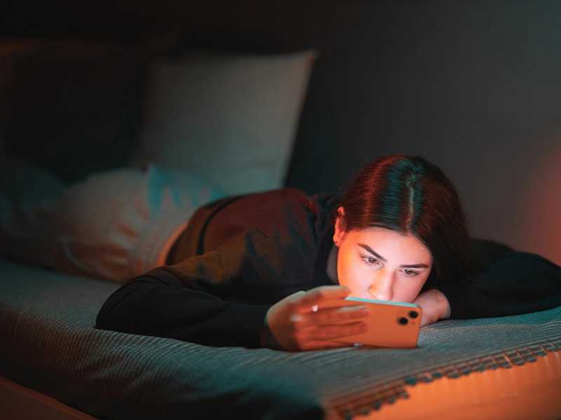 Teenage girl lying in bed looking at her cell phone