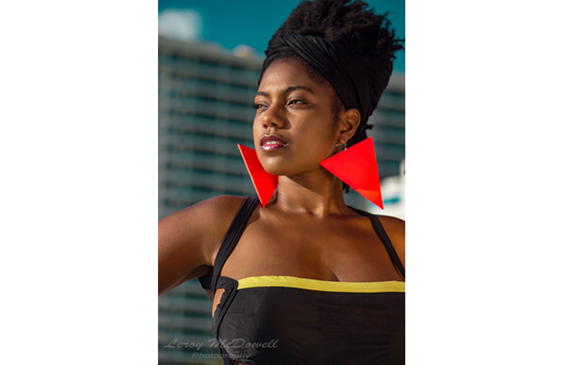 Tranika Dufresne looking towards her right as she poses for an image; she's wearing large red triangle shaped earrings and a black top; image by Leroy McDowell Photgraphy