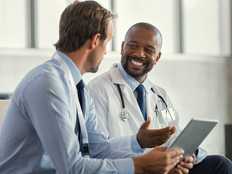 Two doctors sitting and looking at each other while one holds a tablet