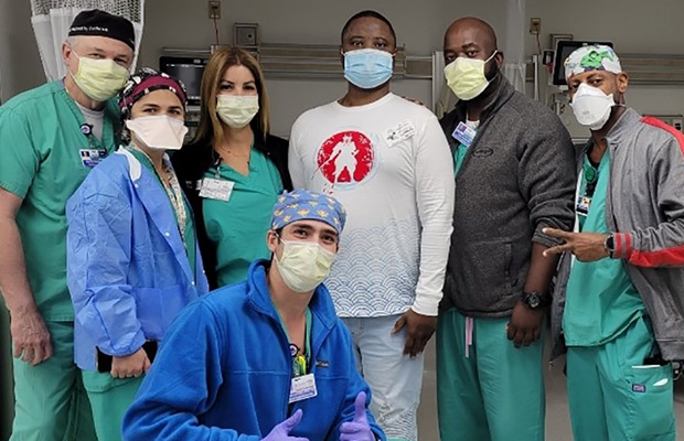 A patient standing in the middle of a group of six medical professionals, they are all wearing face masks and looking at the camera