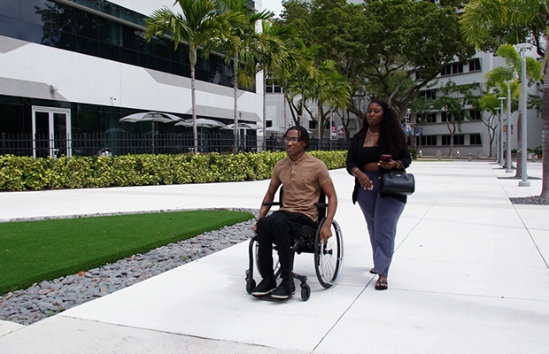 Woman walking alongside a young person in a wheelchair.