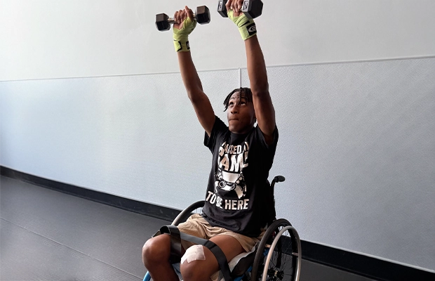 Young person in a wheelchair doing exercises with hand weights.