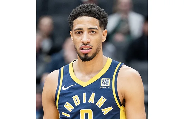 A closeup of a basketball player, he looks towards the camera. He has on a basketball jersey