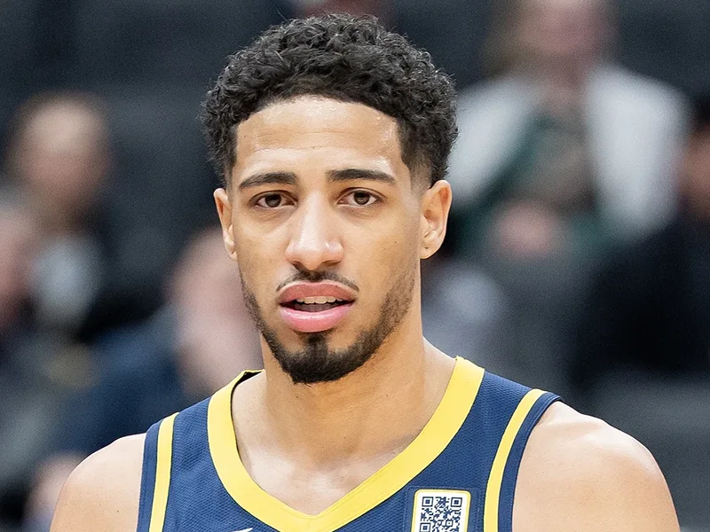 A closeup of a basketball player, he looks towards the camera. He has on a basketball jersey