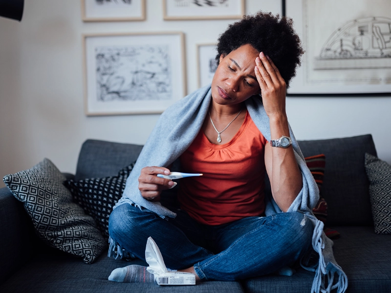 Woman sitting in an armchair covered with a blanket while touching her head as if she had a severe headache