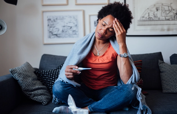 Woman sitting in an armchair covered with a blanket while touching her head as if she had a severe headache