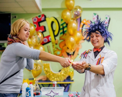 A medical professional wearing a fun purple wig, there's a person next to them doing a science experiment with them
