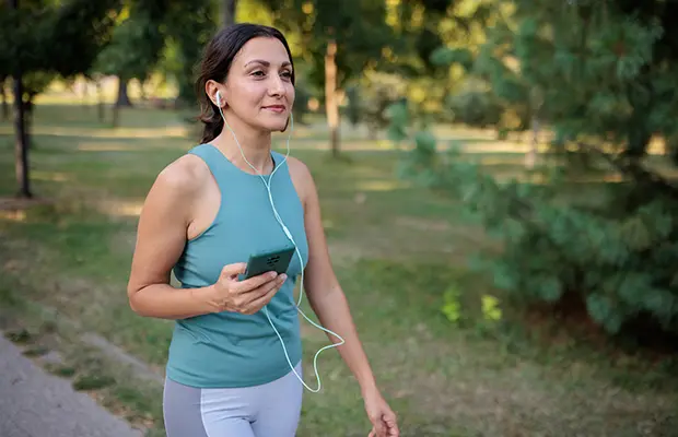 A woman outdoors using her phone with headphones, she has on activewear