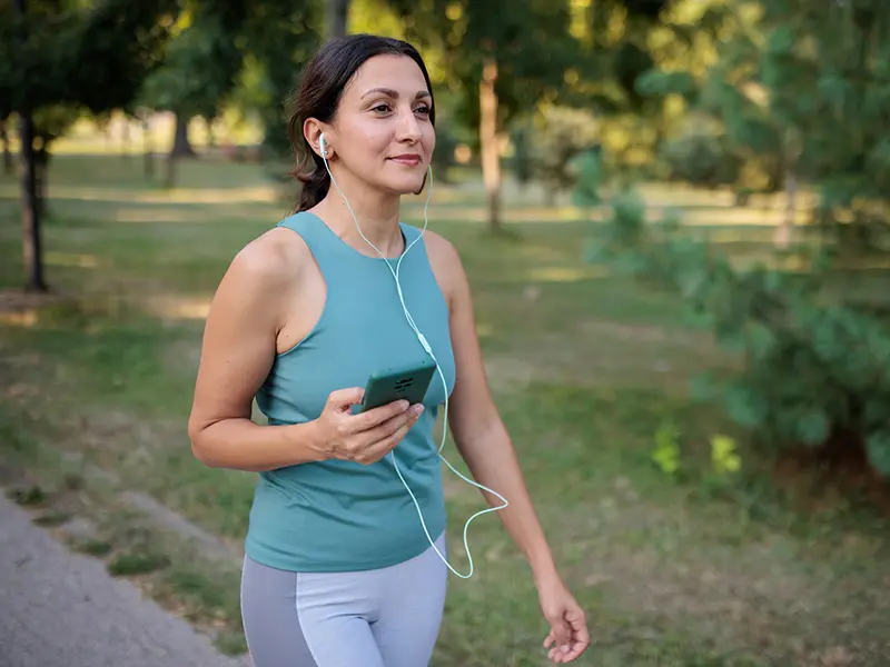 A woman outdoors using her phone with headphones, she has on activewear