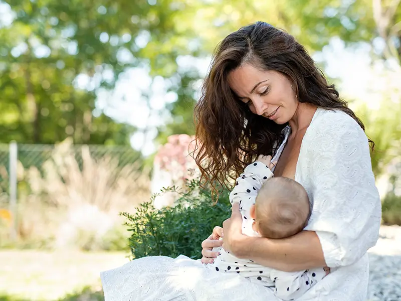 mother feeding her baby sitting in a park