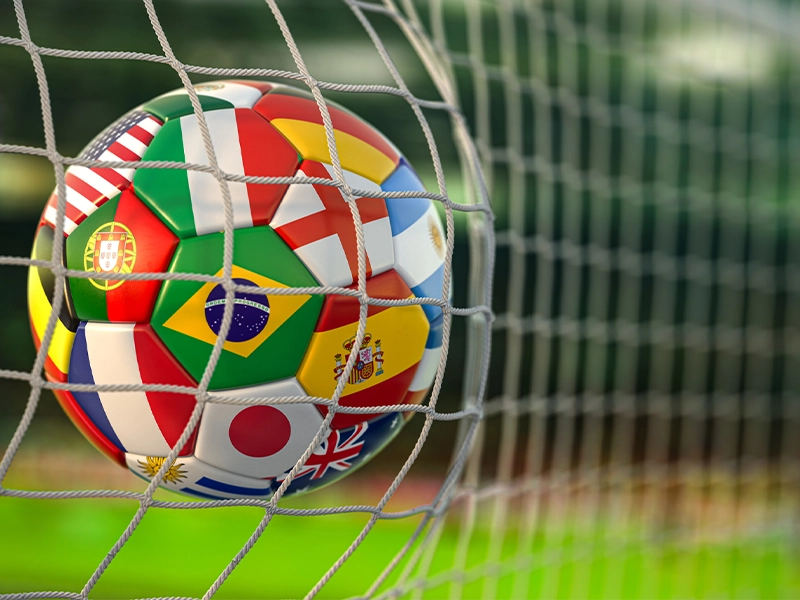 Close-up of a ball printed with all the flags of the world inside the net of a soccer field