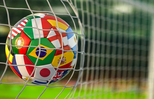 Close-up of a ball printed with all the flags of the world inside the net of a soccer field