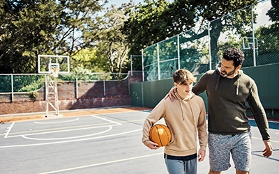 man walking next to his son in a park with basketball courts
