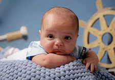 A closeup of a baby, he's laying on a blue blanket and looks at the camera