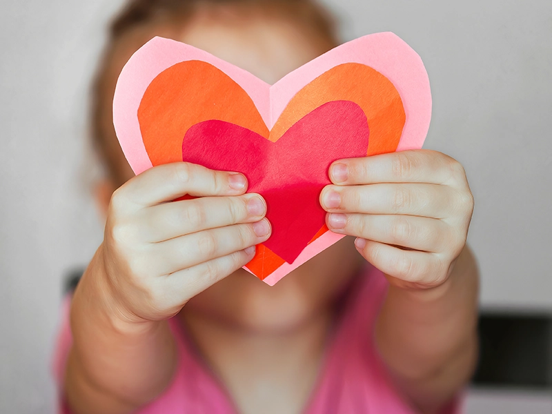 A closeup of a young child holding a cutout of a heart
