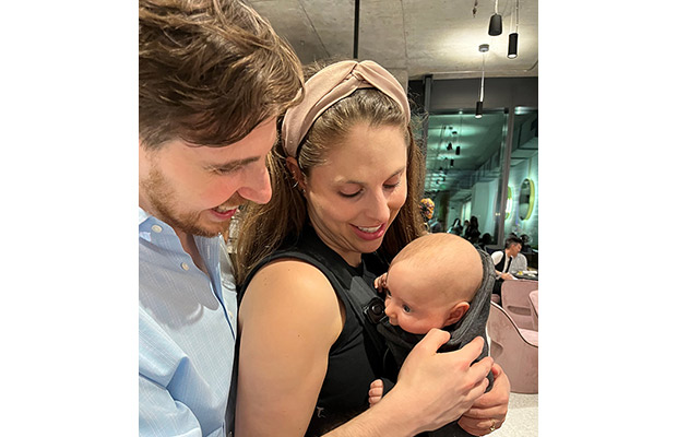 A man and woman holding up a young baby, they look down at the baby and smile