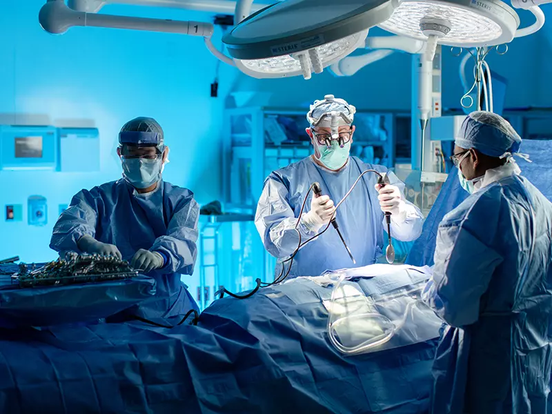 Three surgeons standing around a surgical table as they work on a patients heart