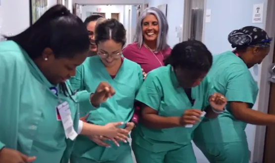 A group of medical professionals smiling, they are dancing in a hallway