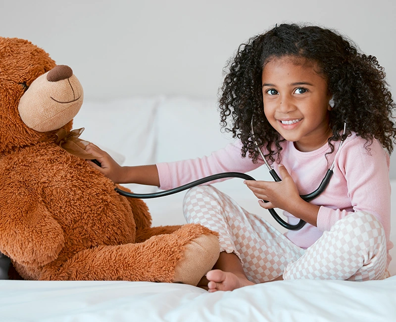 A child playing with a stethoscope and a teddy bear