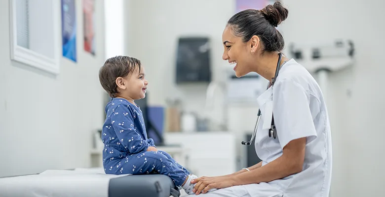 A medical professional smiling at a young patient who is sitting on an examination table