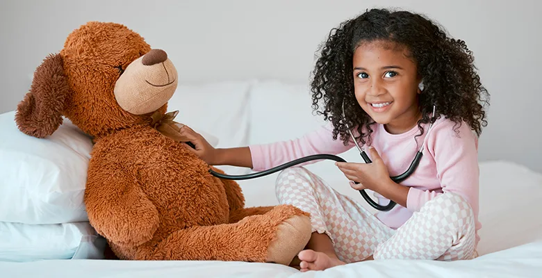 A child playing with a stethoscope and a teddy bear