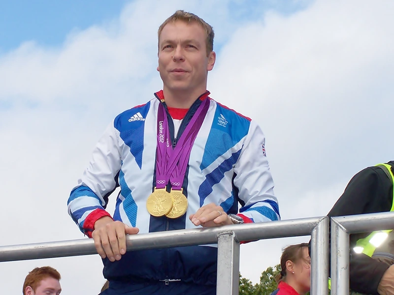 A man standing at a podium looking out, he has two gold Olympic medals around his neck