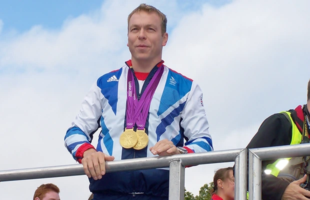 A man standing at a podium looking out, he has two gold Olympic medals around his neck