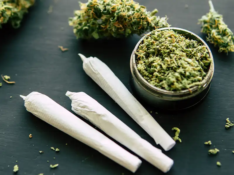 Close-up of two weed cigarettes next to a grinder.