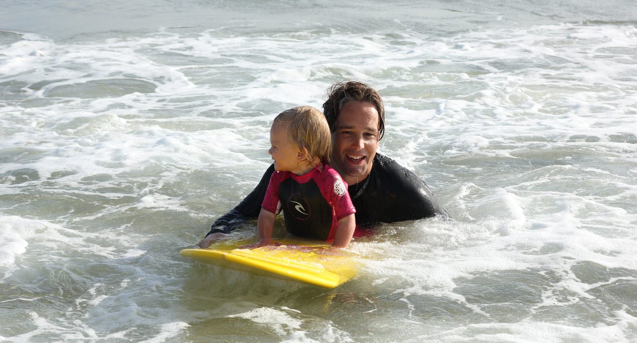 Robert Sabelström på surfbräda i vatten med ett barn