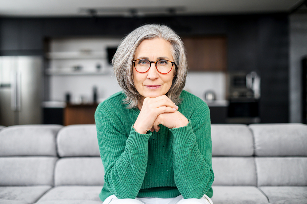 Senior woman sitting on couch with hands on chin