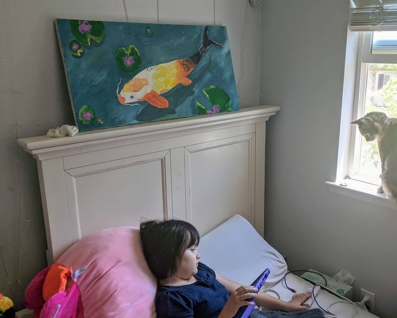 Evelyn watches videos as her recent koi painting sits overhead.