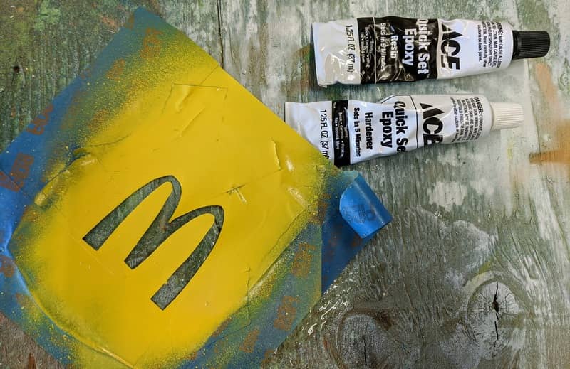 The free hand cut stencil of the McDonald's golden arch sits coated in yellow paint.