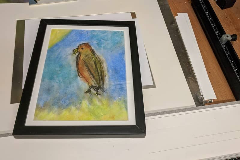 A framed sketch of a bird made by Isabella during the pandemic sits on the matte cutter.