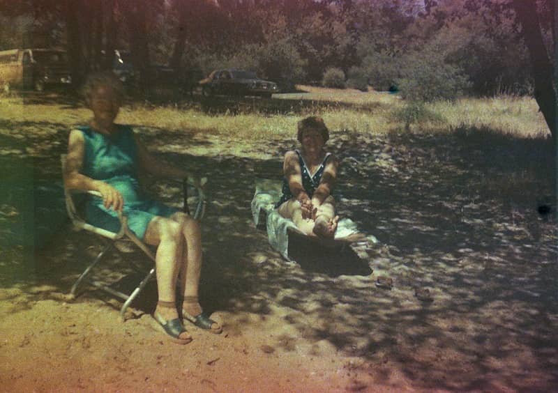 Found film: two women sit along the shore in the shade in what appears to the California foothills.