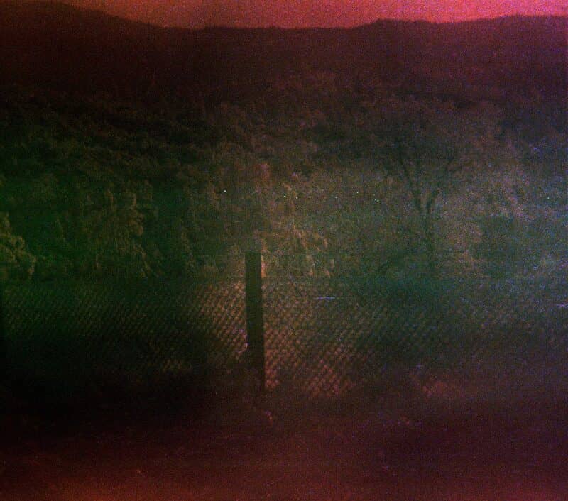 Found film: a single fence post over what appears to be a valley.