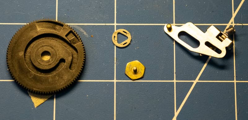 From left: the focus wheel (reversed), the focus wheel pivot, the focus wheel retaining screw, cam follower assembly with spring.