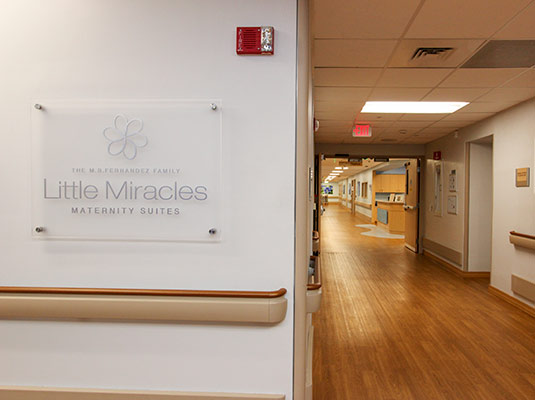 A hospital hallway with a sign that reads Little Miracles Maternity Suites