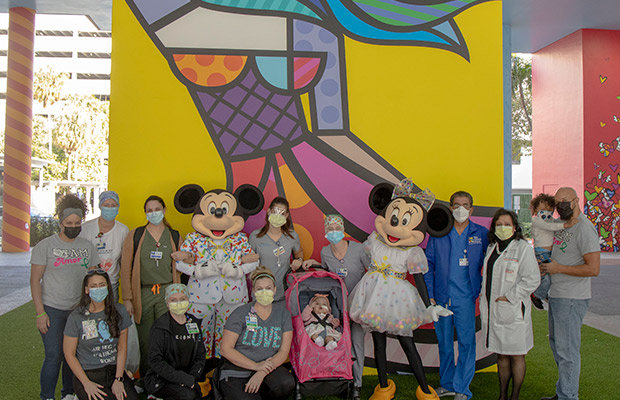 Baby outdoors surrounded by medical professionals and two Disney characters