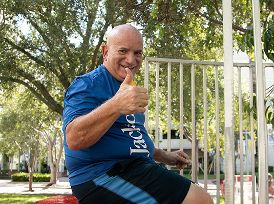 A man sitting outdoors, he giving the thumbs up to the camera